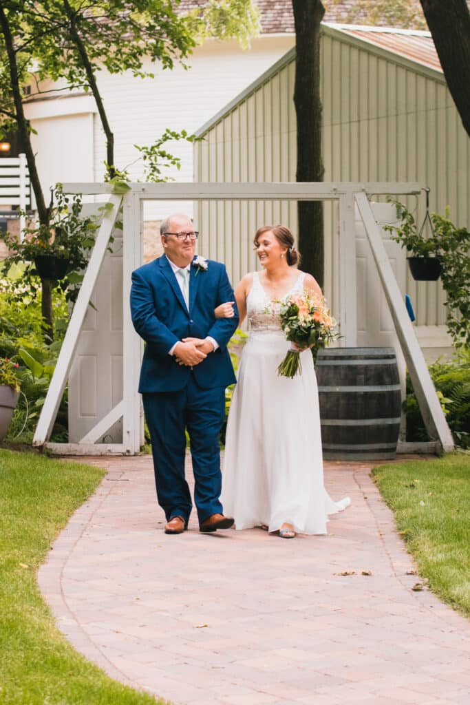 Father walking his daughter, the Bride down the beautiful paved ceremony aisle at one of the best Minnesota Wedding Venues Round Barn Farm in Red Wing.