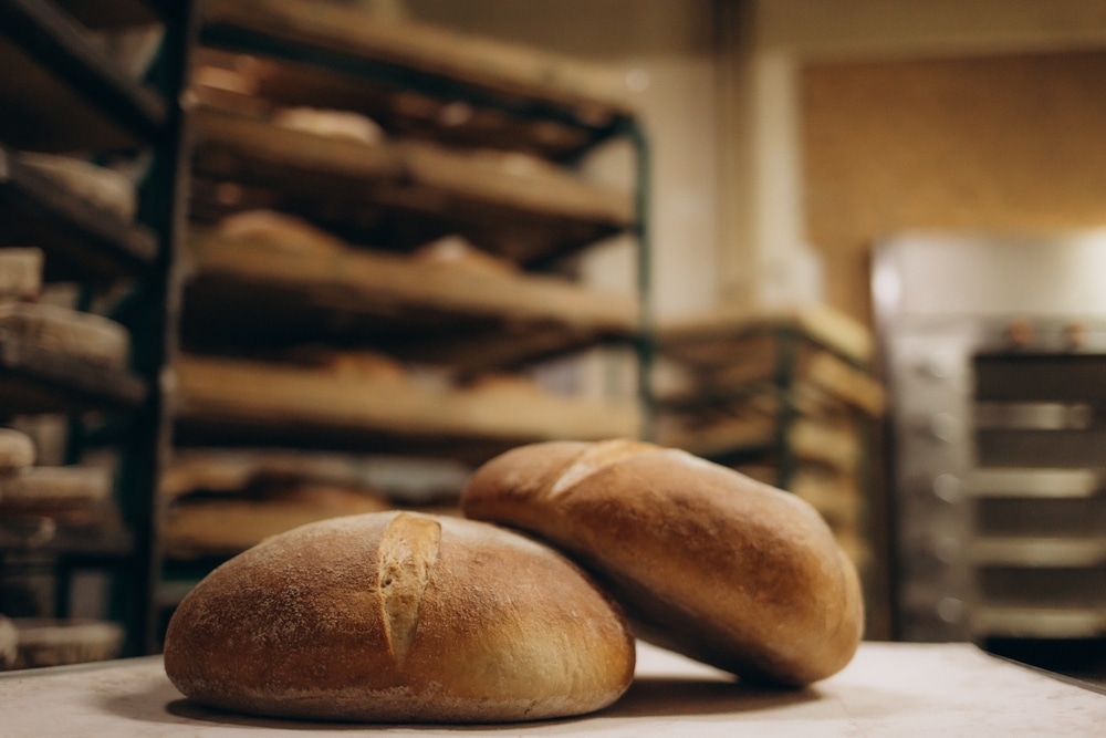 Have a Cozy Visit to Hanisch Bakery in Red Wing, MN 4 Two loaves of round bread in foreground, racks of bread waiting at Hanisch Bakery.